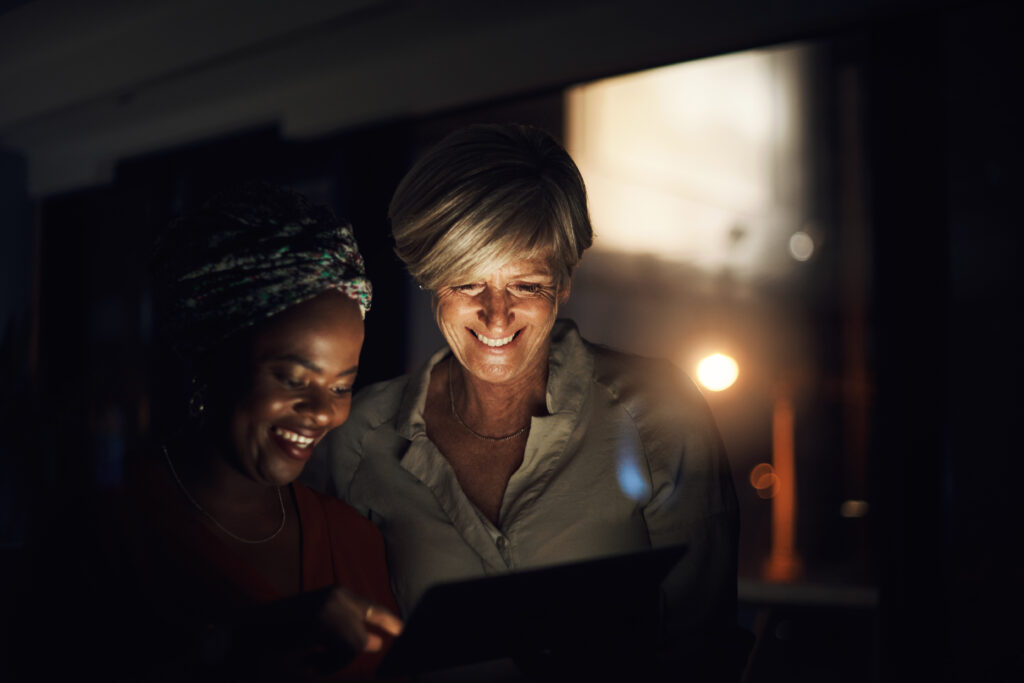 Shot of two businesswomen using a digital tablet together in an office at night.